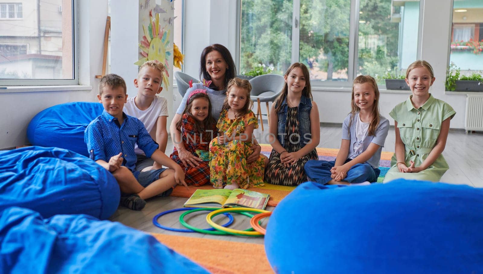 A happy female teacher sitting and playing hand games with a group of little schoolchildren.