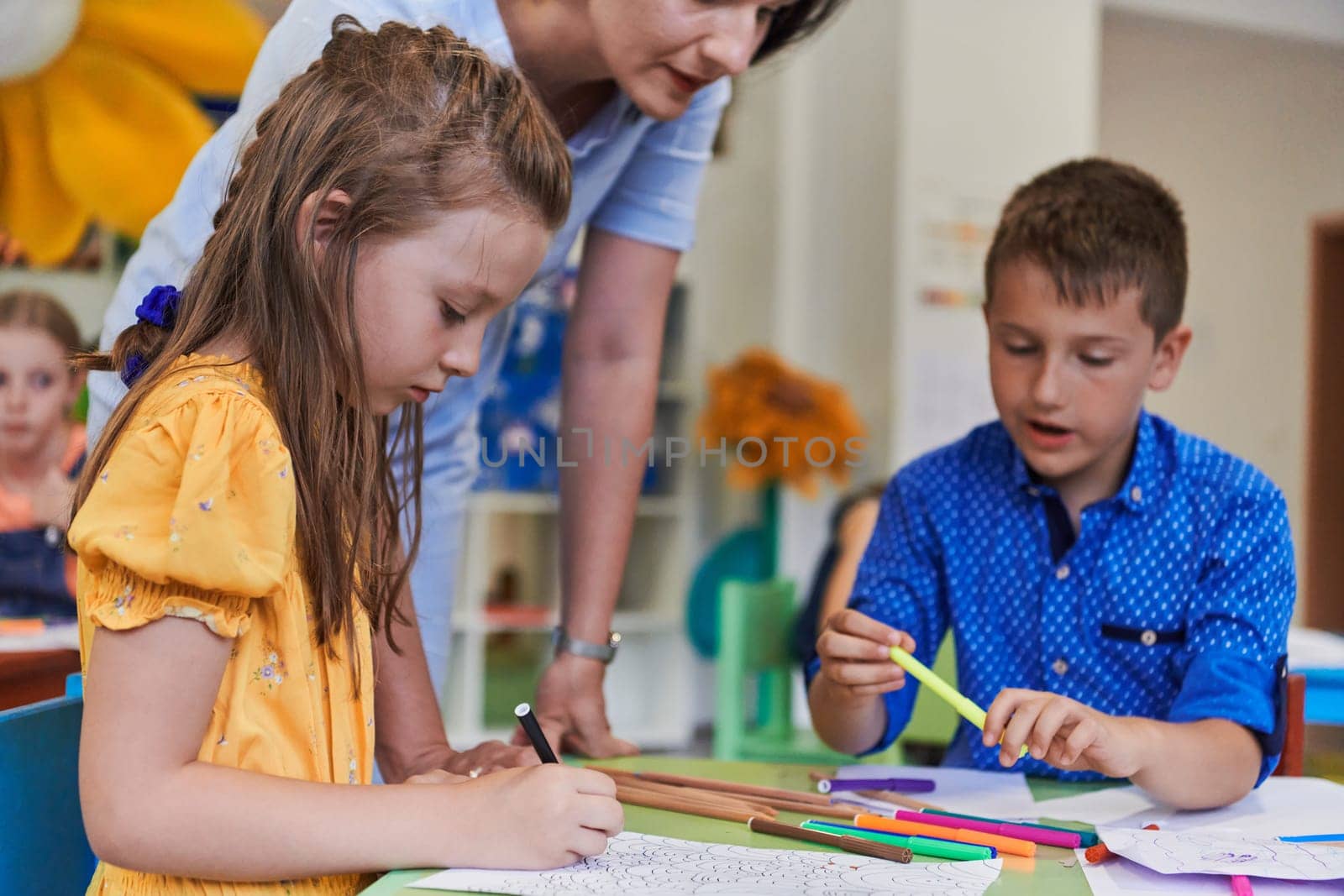 Creative kids during an art class in a daycare center or elementary school classroom drawing with female teacher