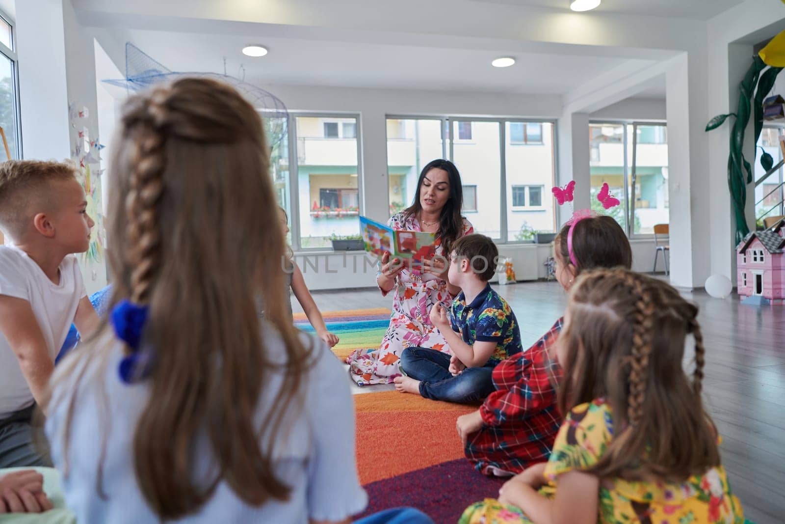 Reading time in an elementary school or kindergarten, a teacher reading a book to children in an elementary school or kindergarten. The concept of pre-school education. Selective focus by dotshock