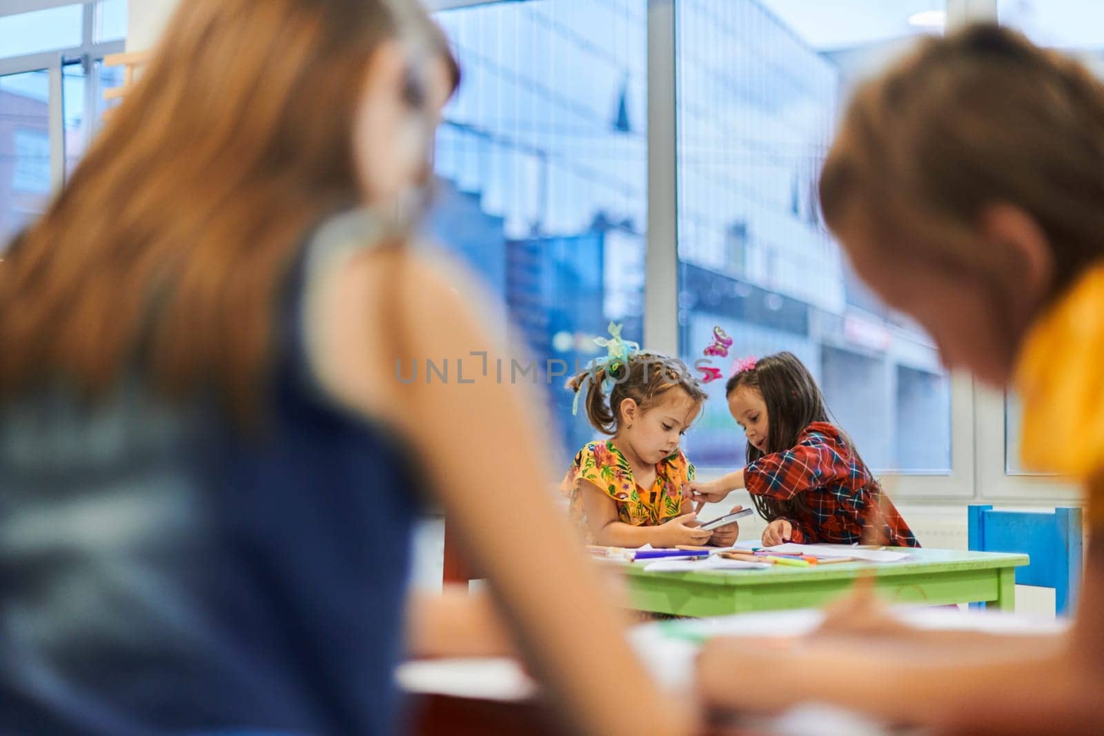 Creative kids during an art class in a daycare center or elementary school classroom drawing with female teacher