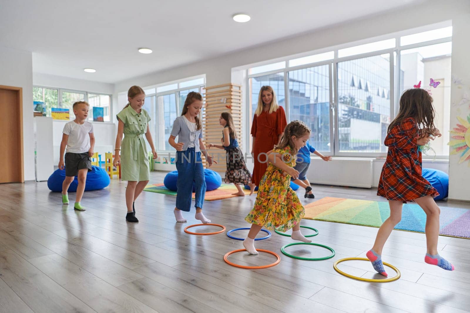 Small nursery school children with female teacher on floor indoors in classroom, doing exercise. Jumping over hula hoop circles track on the floor. by dotshock