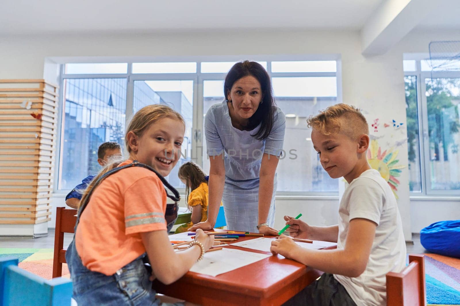 Creative kids during an art class in a daycare center or elementary school classroom drawing with female teacher