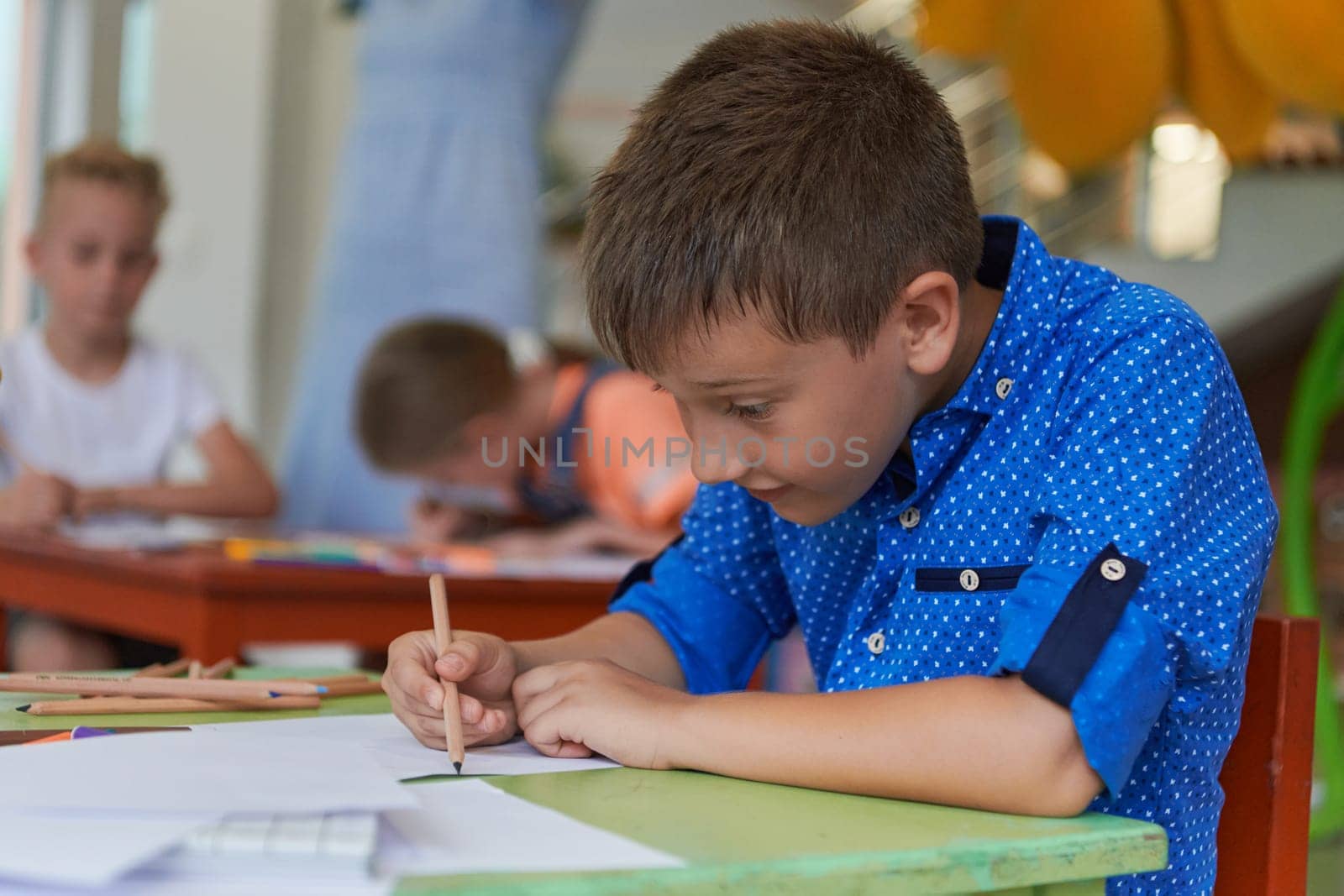 A boy at a preschool institution sits and draws in a notebook with a smile on his face. High quality photo