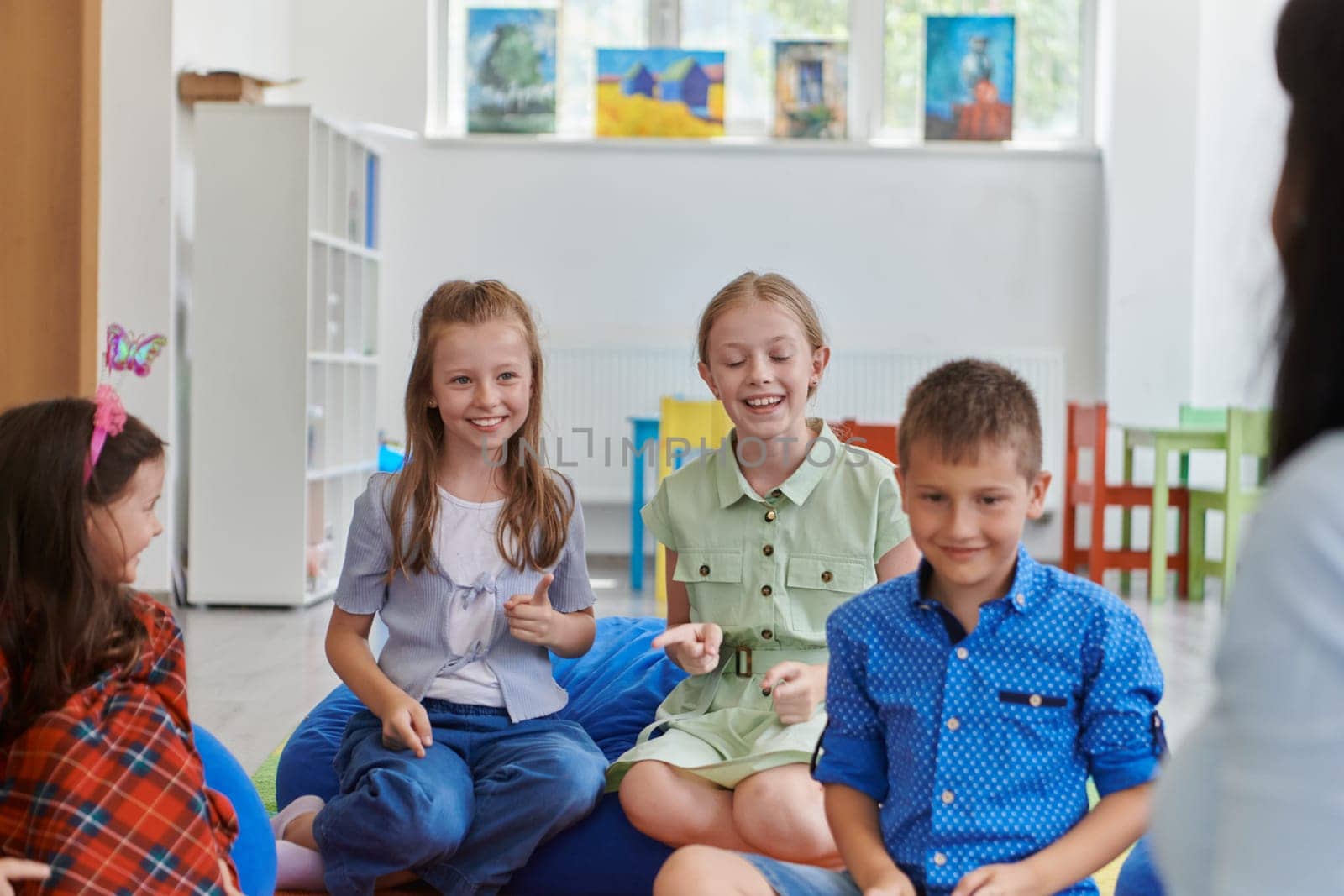 A happy female teacher sitting and playing hand games with a group of little schoolchildren by dotshock