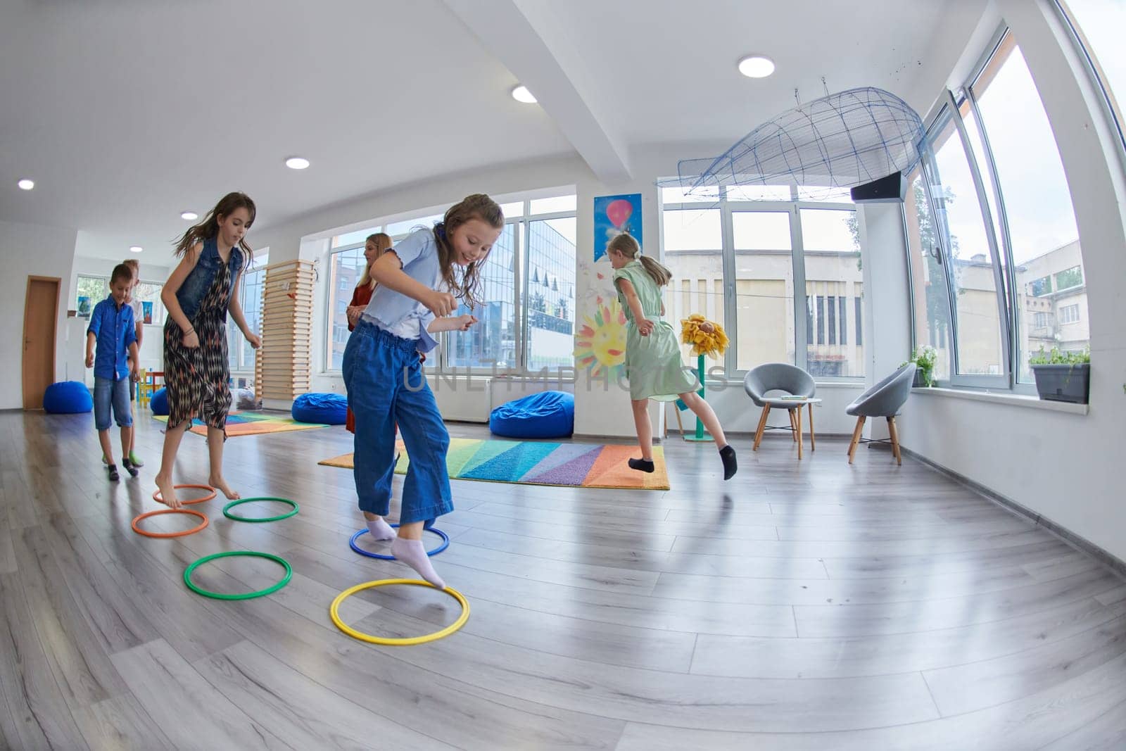 Small nursery school children with female teacher on floor indoors in classroom, doing exercise. Jumping over hula hoop circles track on the floor. by dotshock