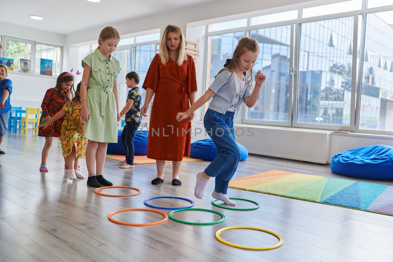 Small nursery school children with female teacher on floor indoors in classroom, doing exercise. Jumping over hula hoop circles track on the floor. by dotshock