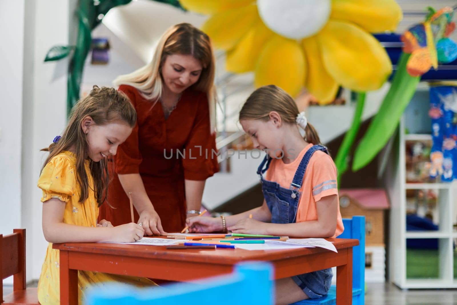 Creative kids during an art class in a daycare center or elementary school classroom drawing with female teacher. by dotshock