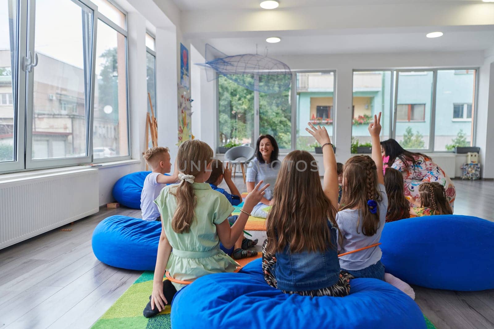 A happy female teacher sitting and playing hand games with a group of little schoolchildren by dotshock