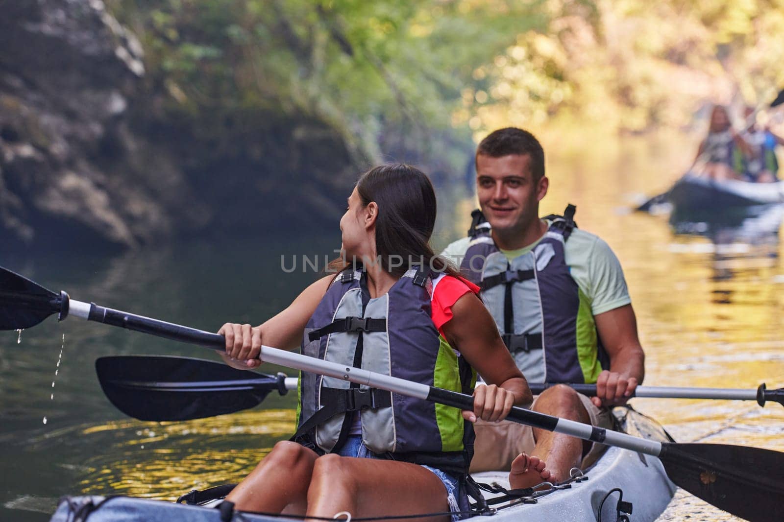 A group of friends enjoying having fun and kayaking while exploring the calm river, surrounding forest and large natural river canyons.