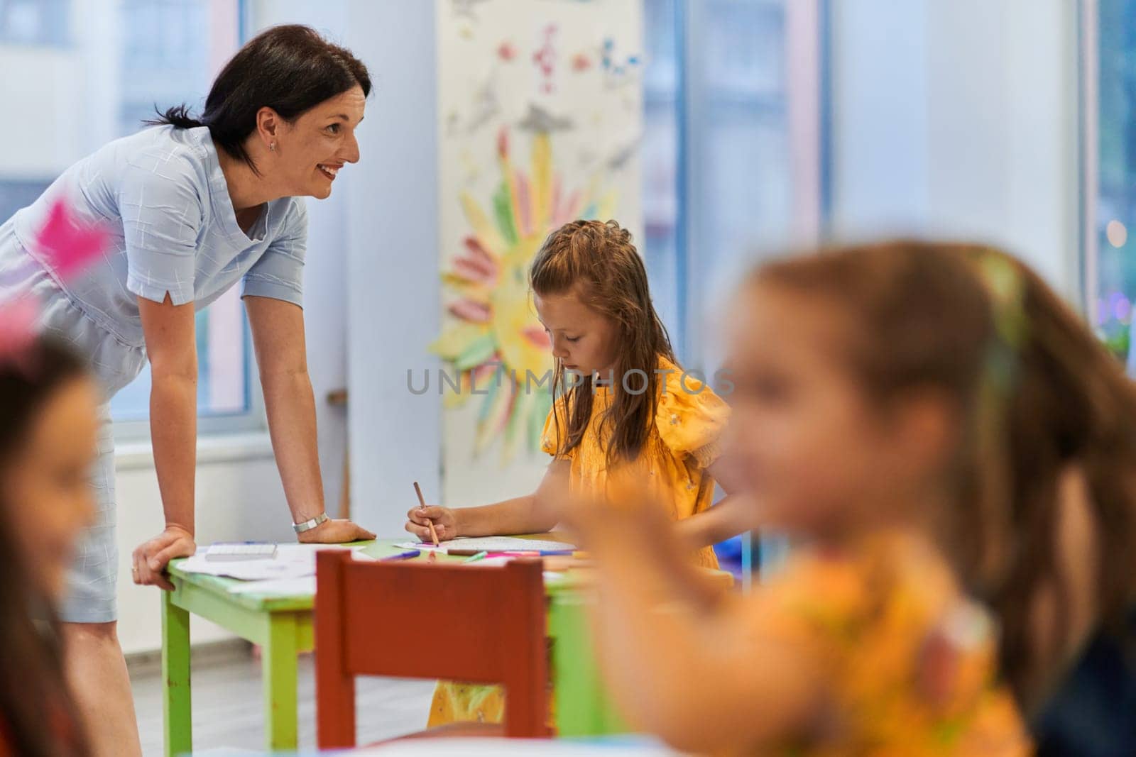 Creative kids during an art class in a daycare center or elementary school classroom drawing with female teacher