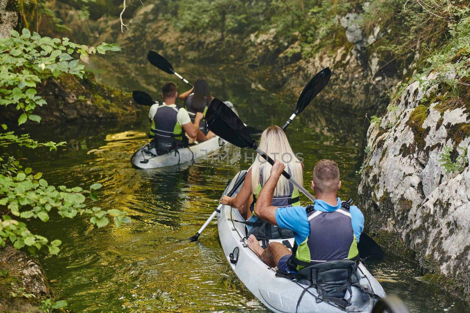 A group of friends enjoying having fun and kayaking while exploring the calm river, surrounding forest and large natural river canyons by dotshock