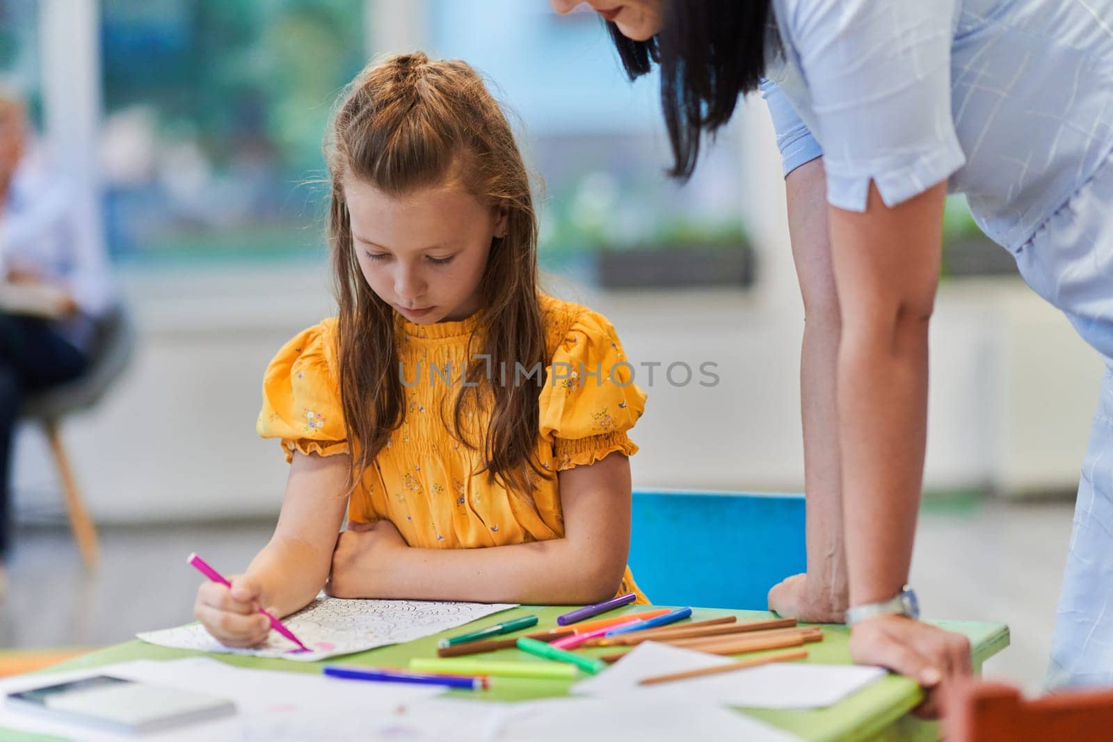 Creative kids during an art class in a daycare center or elementary school classroom drawing with female teacher