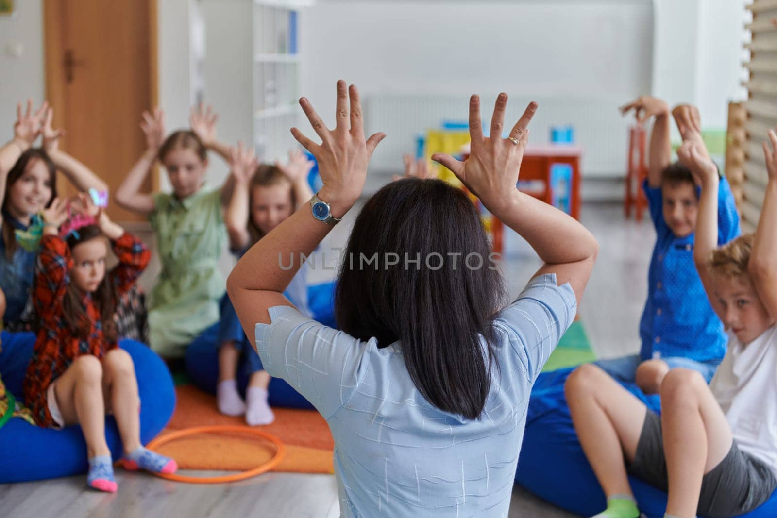 A happy female teacher sitting and playing hand games with a group of little schoolchildren.