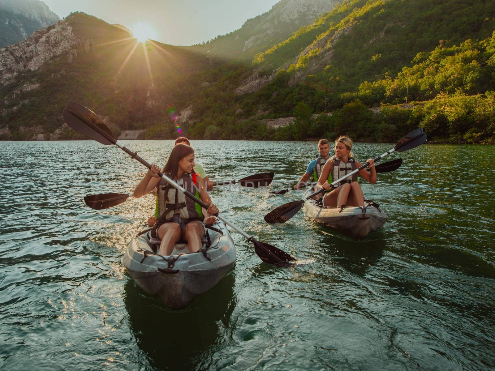 A group of friends enjoying fun and kayaking exploring the calm river, surrounding forest and large natural river canyons during an idyllic sunset. by dotshock