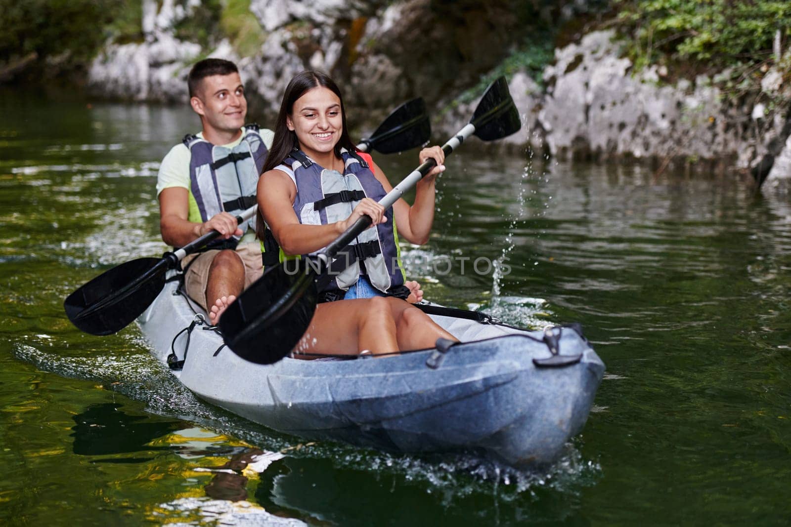 A young couple enjoying an idyllic kayak ride in the middle of a beautiful river surrounded by forest greenery.