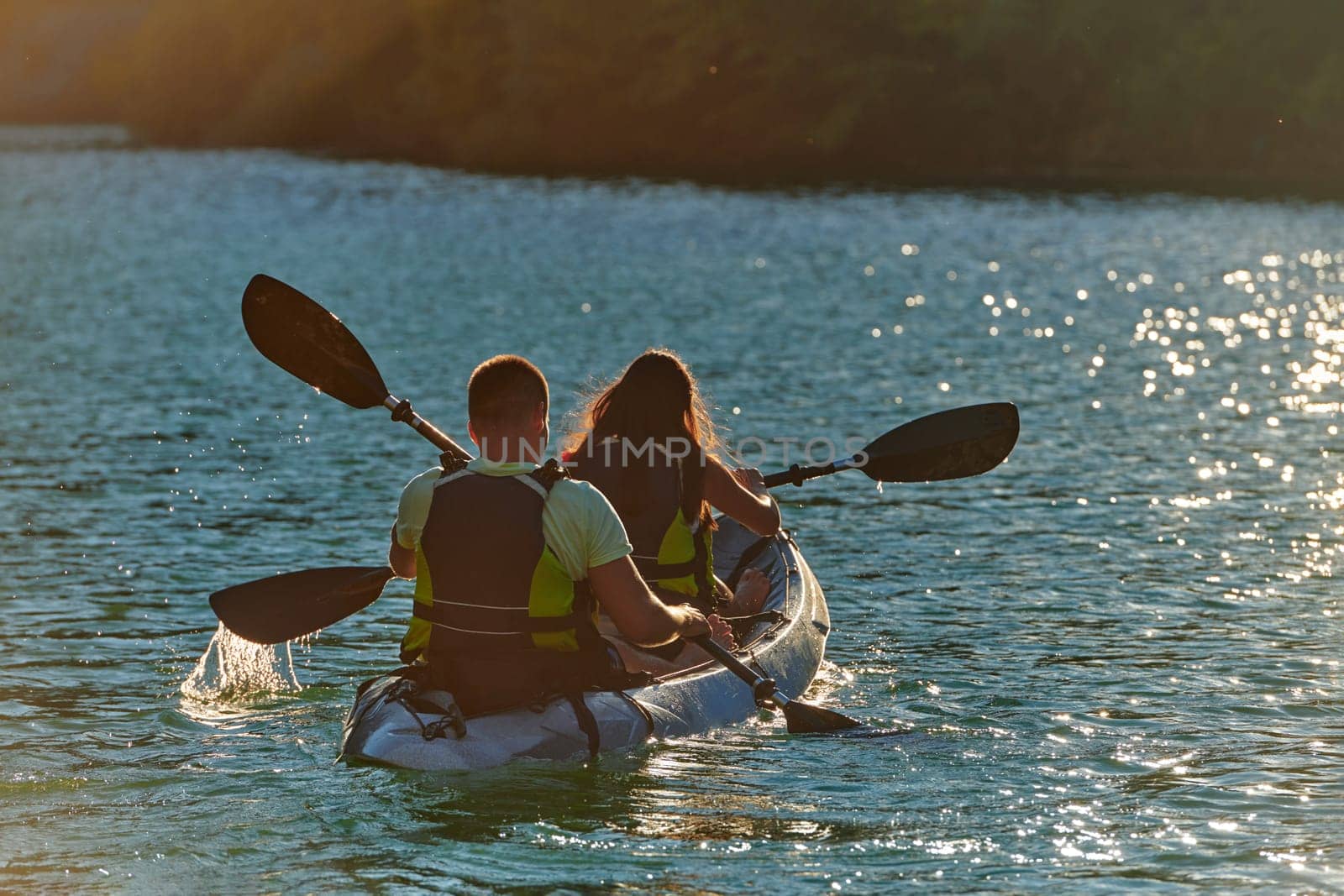 A young couple enjoying an idyllic kayak ride in the middle of a beautiful river surrounded by forest greenery in sunset time by dotshock