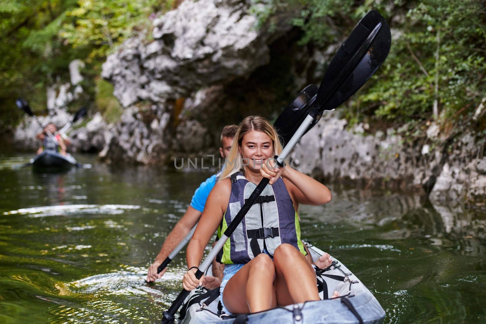 A group of friends enjoying having fun and kayaking while exploring the calm river, surrounding forest and large natural river canyons.