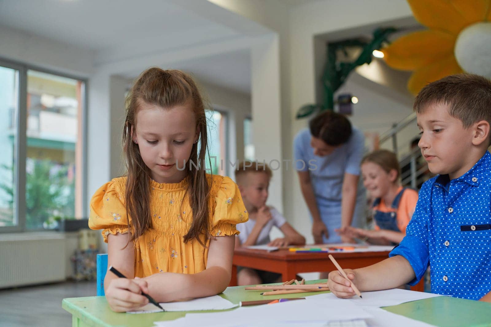 Creative kids during an art class in a daycare center or elementary school classroom drawing with female teacher