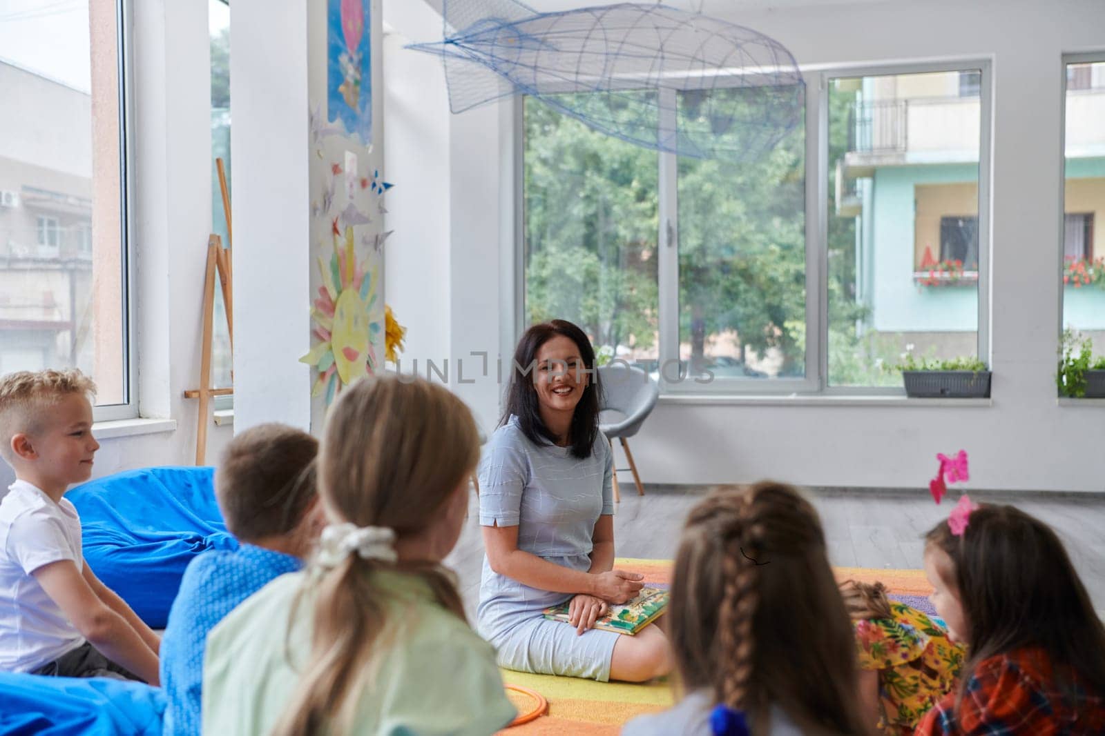 A happy female teacher sitting and playing hand games with a group of little schoolchildren.