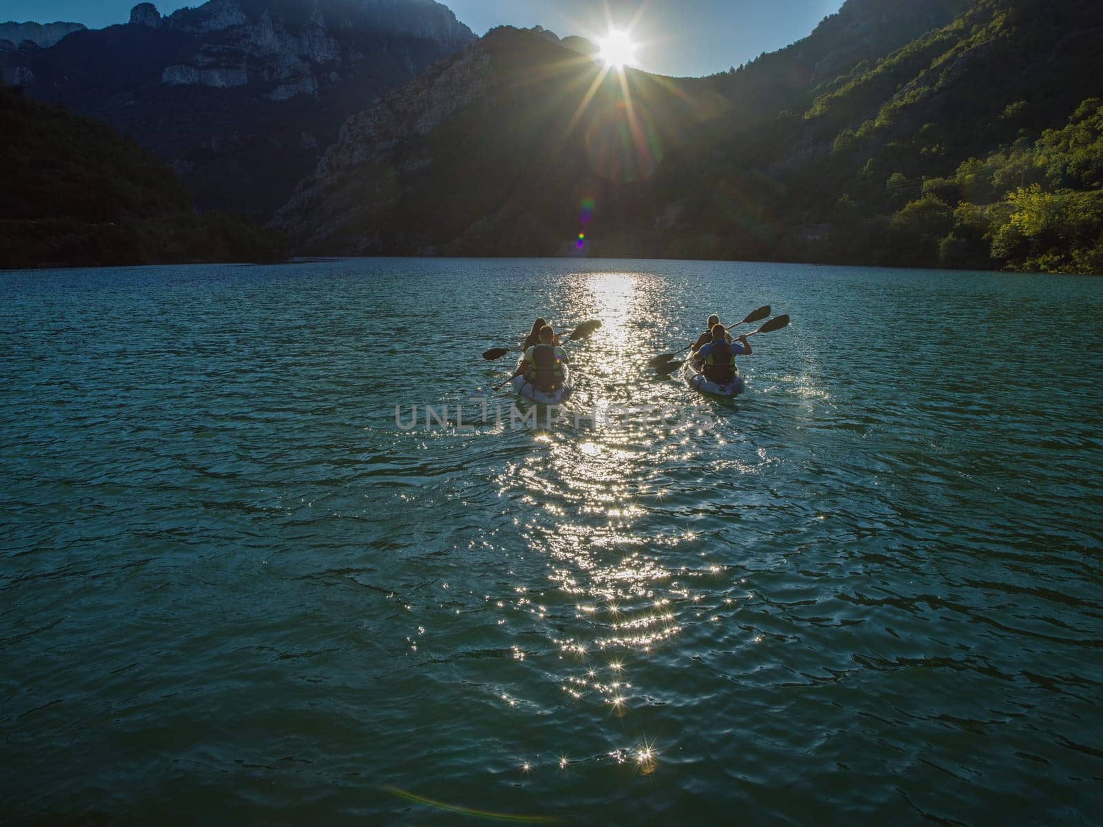 A group of friends enjoying fun and kayaking exploring the calm river, surrounding forest and large natural river canyons during an idyllic sunset