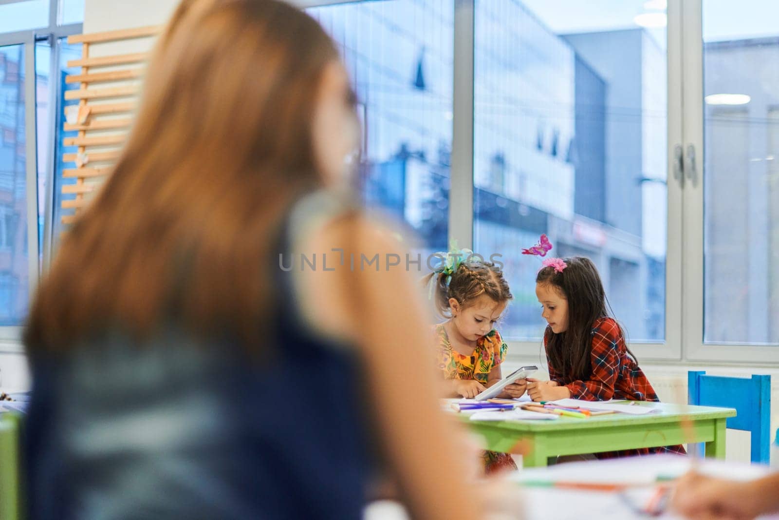 Creative kids during an art class in a daycare center or elementary school classroom drawing with female teacher