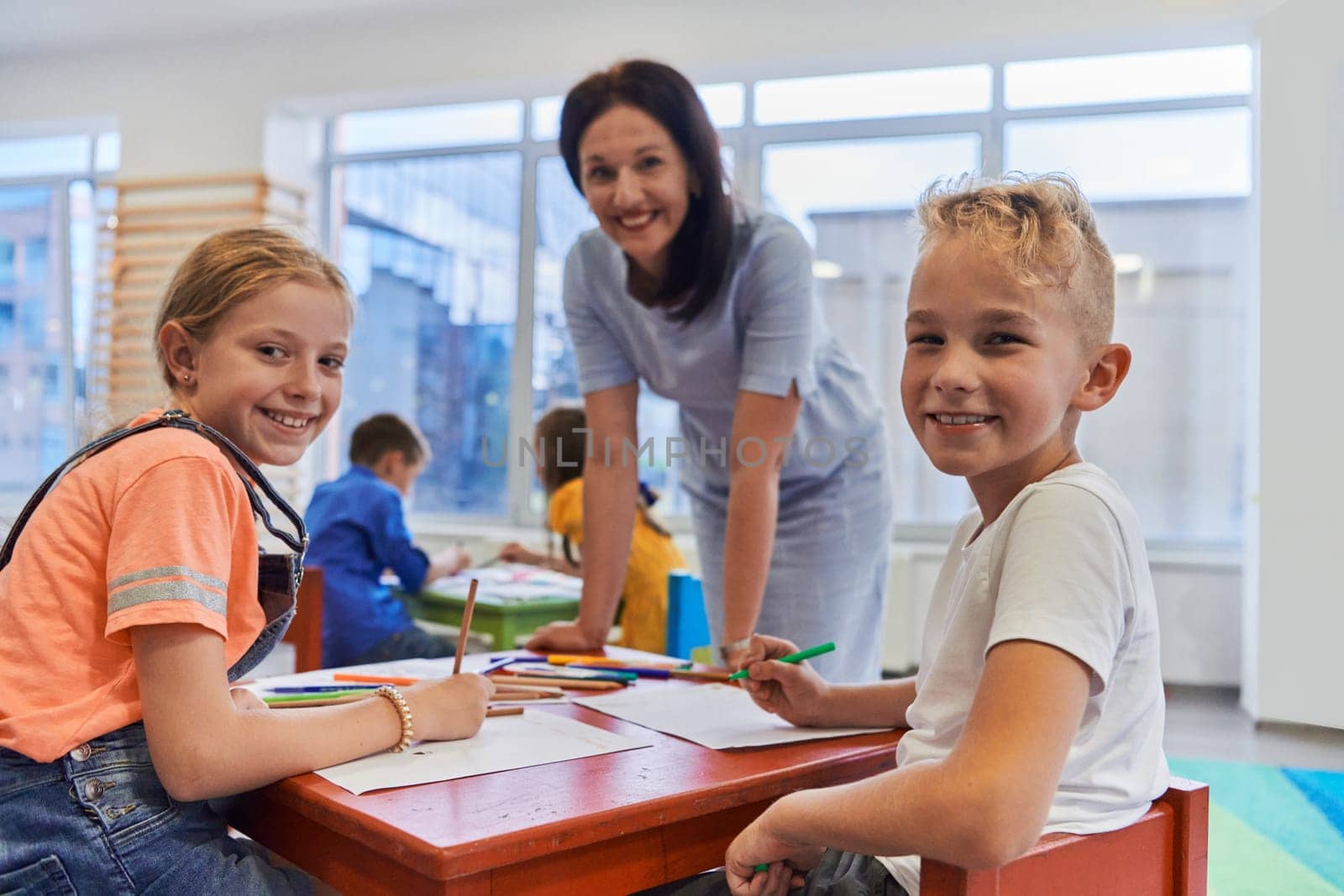 Creative kids during an art class in a daycare center or elementary school classroom drawing with female teacher