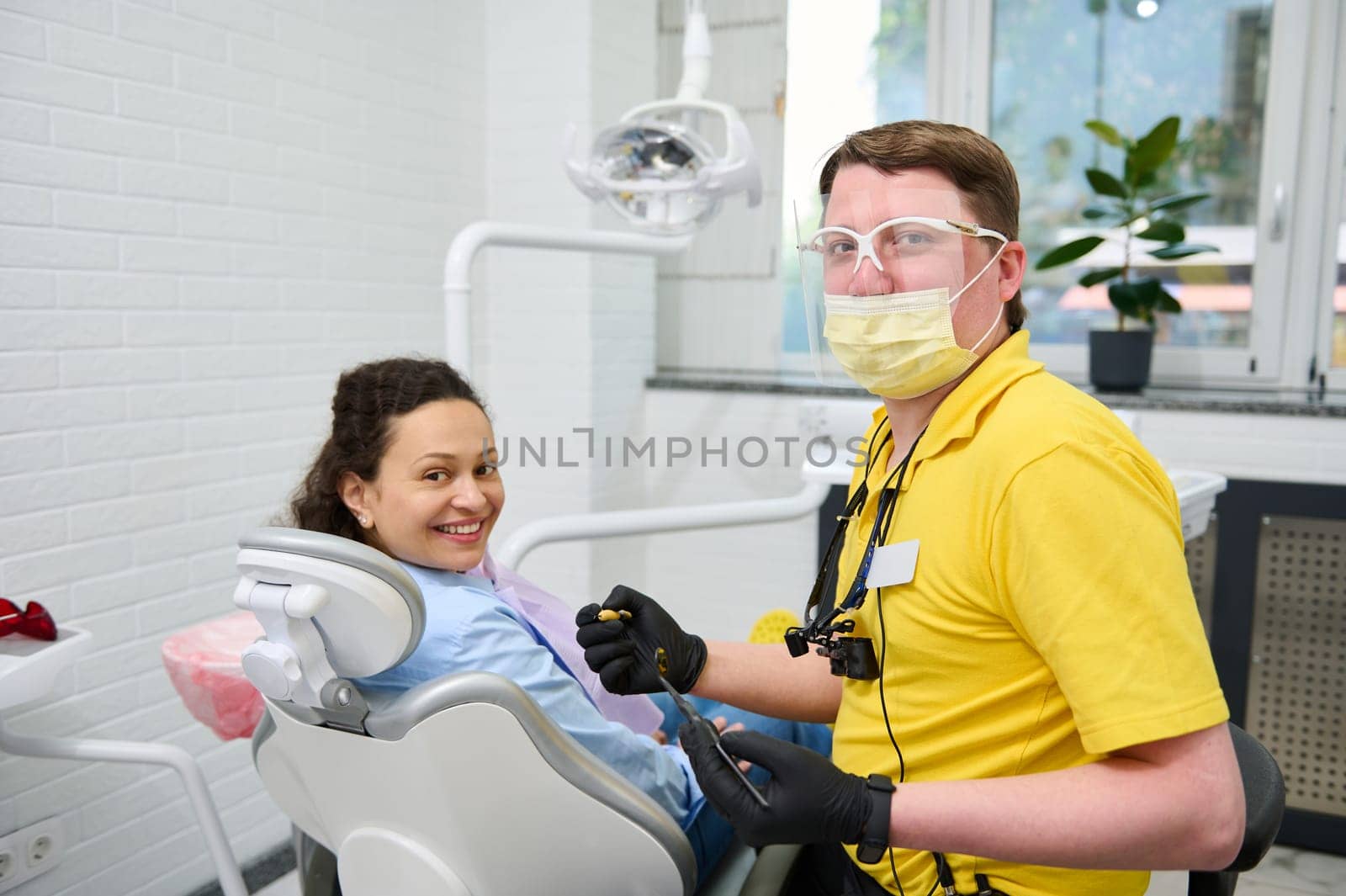 Competent male dentist doctor and happy woman patient, smiling looking at camera. Pregnant woman at dental appointment by artgf