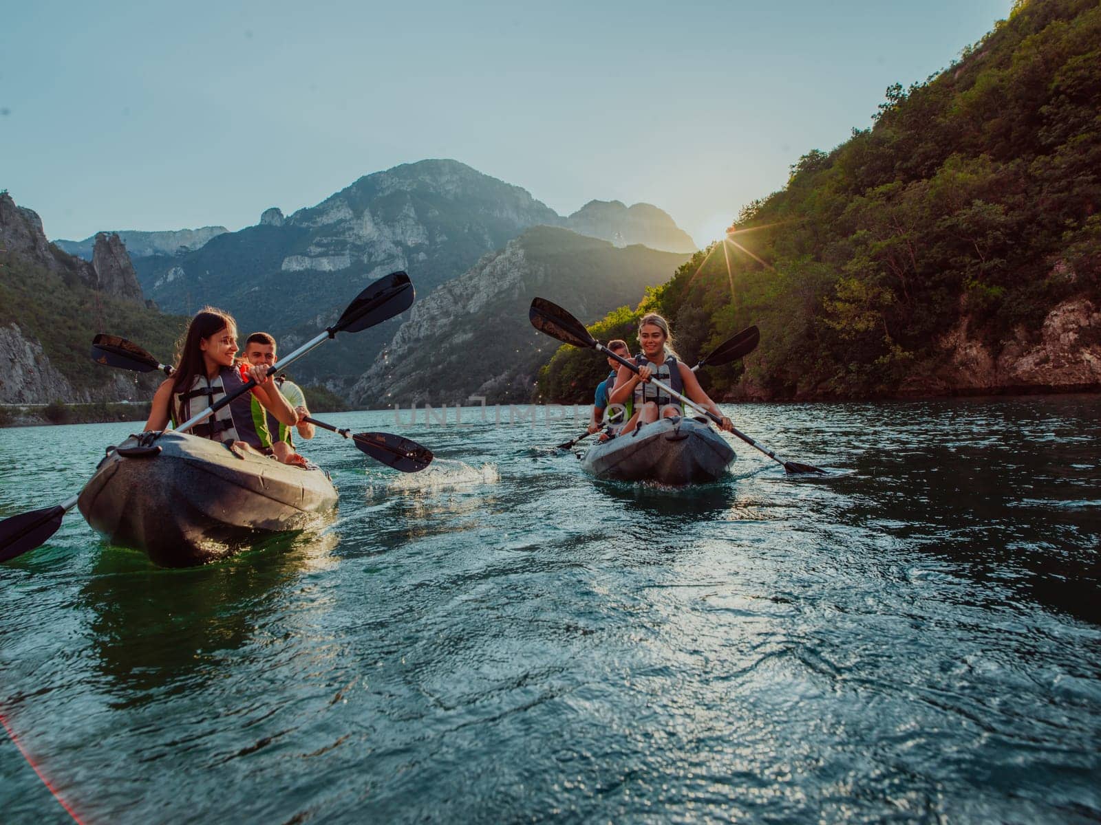 A group of friends enjoying fun and kayaking exploring the calm river, surrounding forest and large natural river canyons during an idyllic sunset. by dotshock