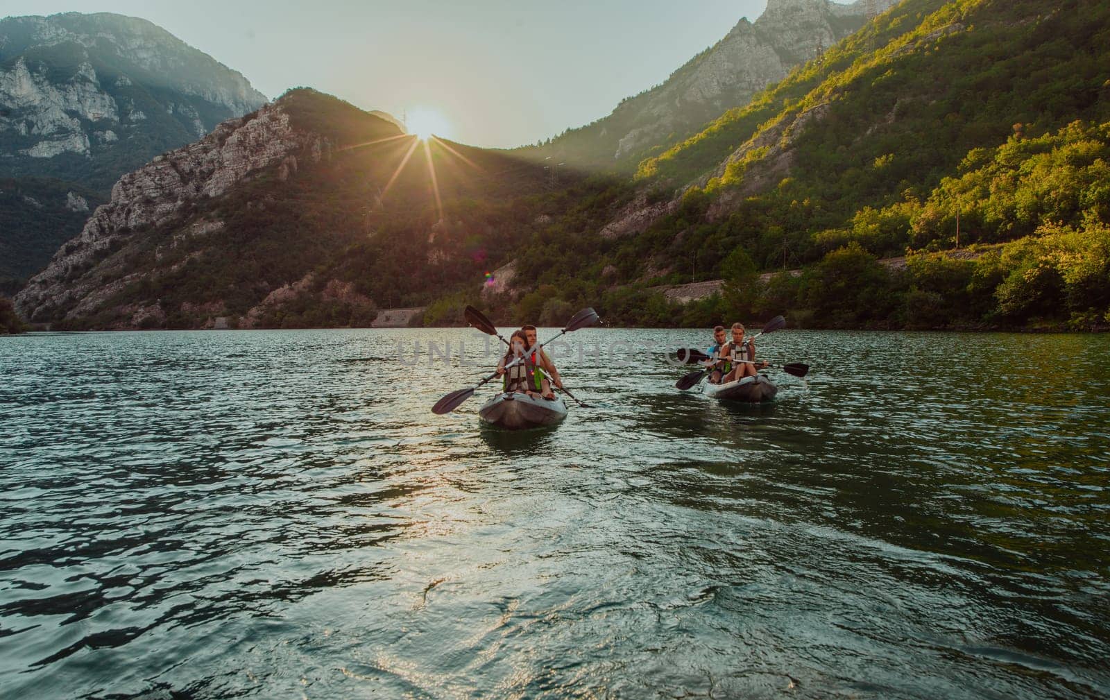 A group of friends enjoying fun and kayaking exploring the calm river, surrounding forest and large natural river canyons during an idyllic sunset. by dotshock