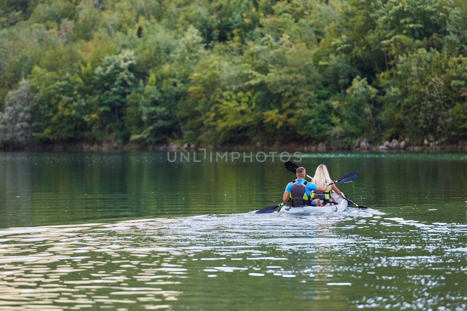 A young couple enjoying an idyllic kayak ride in the middle of a beautiful river surrounded by forest greenery by dotshock