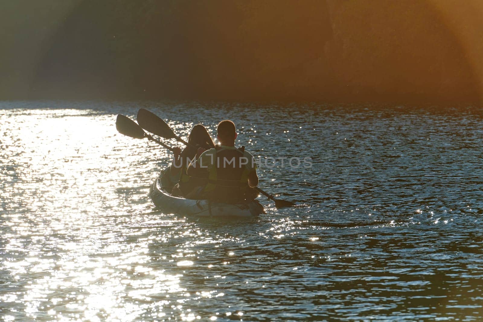 A young couple enjoying an idyllic kayak ride in the middle of a beautiful river surrounded by forest greenery in sunset time.