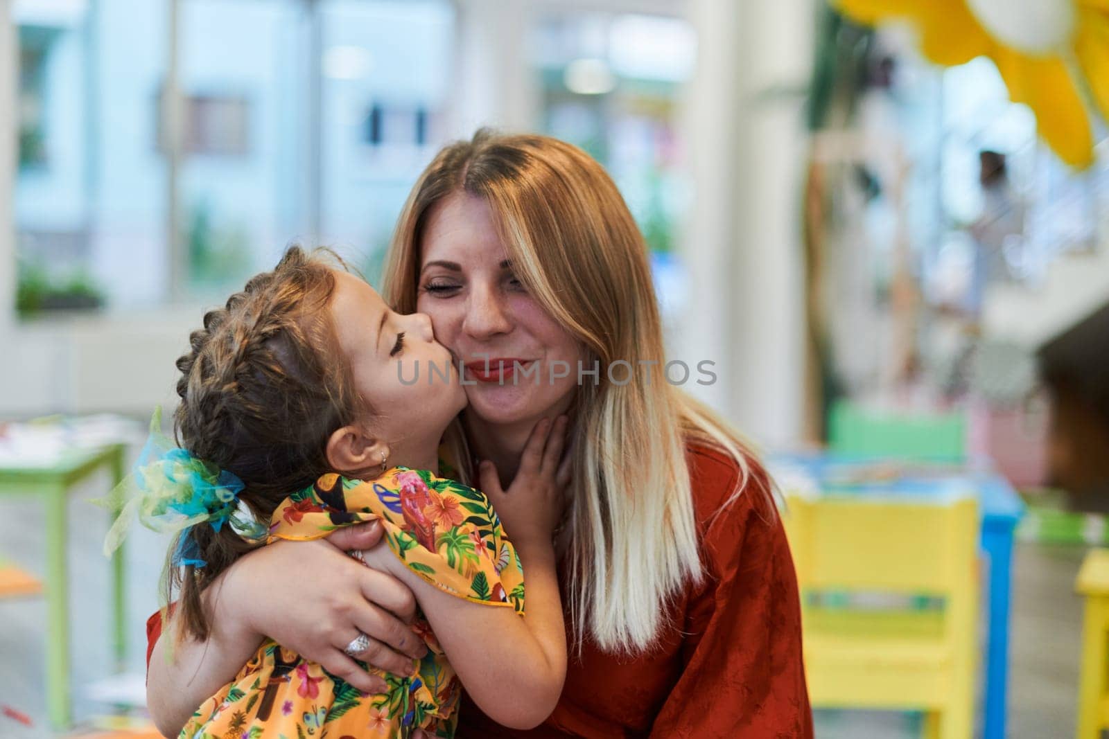 A cute little girl kissing and hugs her mother in preschool. High quality photo