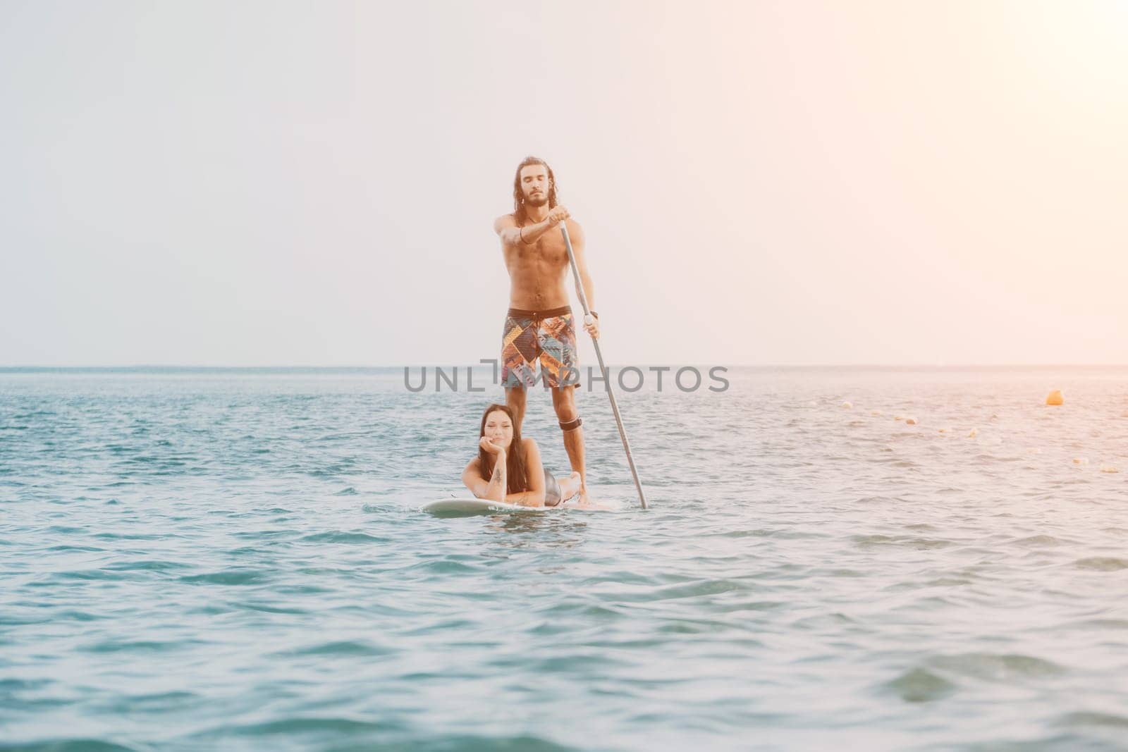 Sea woman and man on sup. Silhouette of happy young woman and man, surfing on SUP board, confident paddling through water surface. Idyllic sunset. Active lifestyle at sea or river. Slow motion by panophotograph