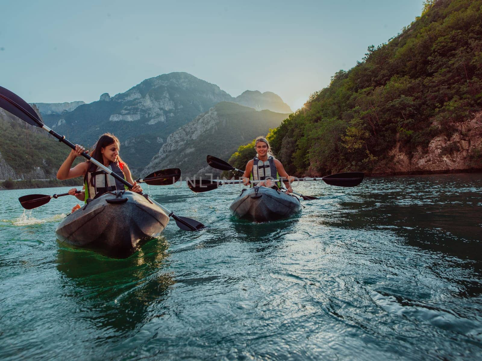 A group of friends enjoying fun and kayaking exploring the calm river, surrounding forest and large natural river canyons during an idyllic sunset