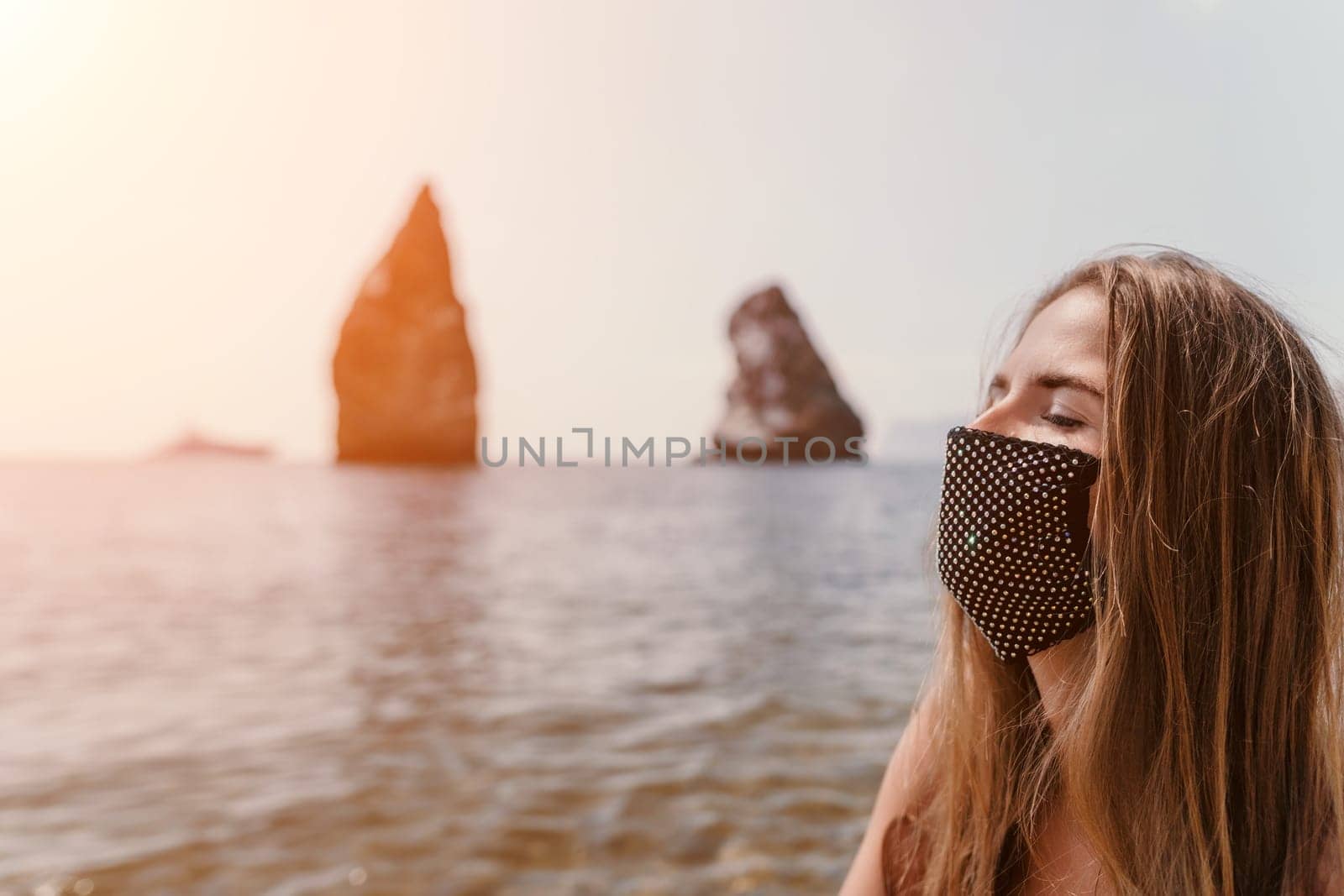 Woman travel sea. Young Happy woman in a long red dress posing on a beach near the sea on background of volcanic rocks, like in Iceland, sharing travel adventure journey