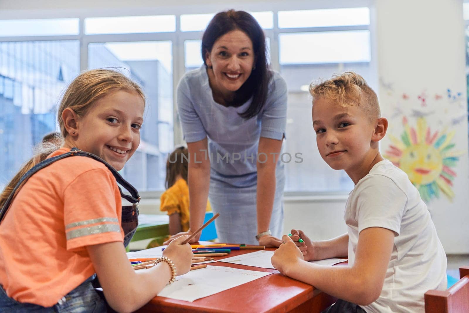 Creative kids during an art class in a daycare center or elementary school classroom drawing with female teacher