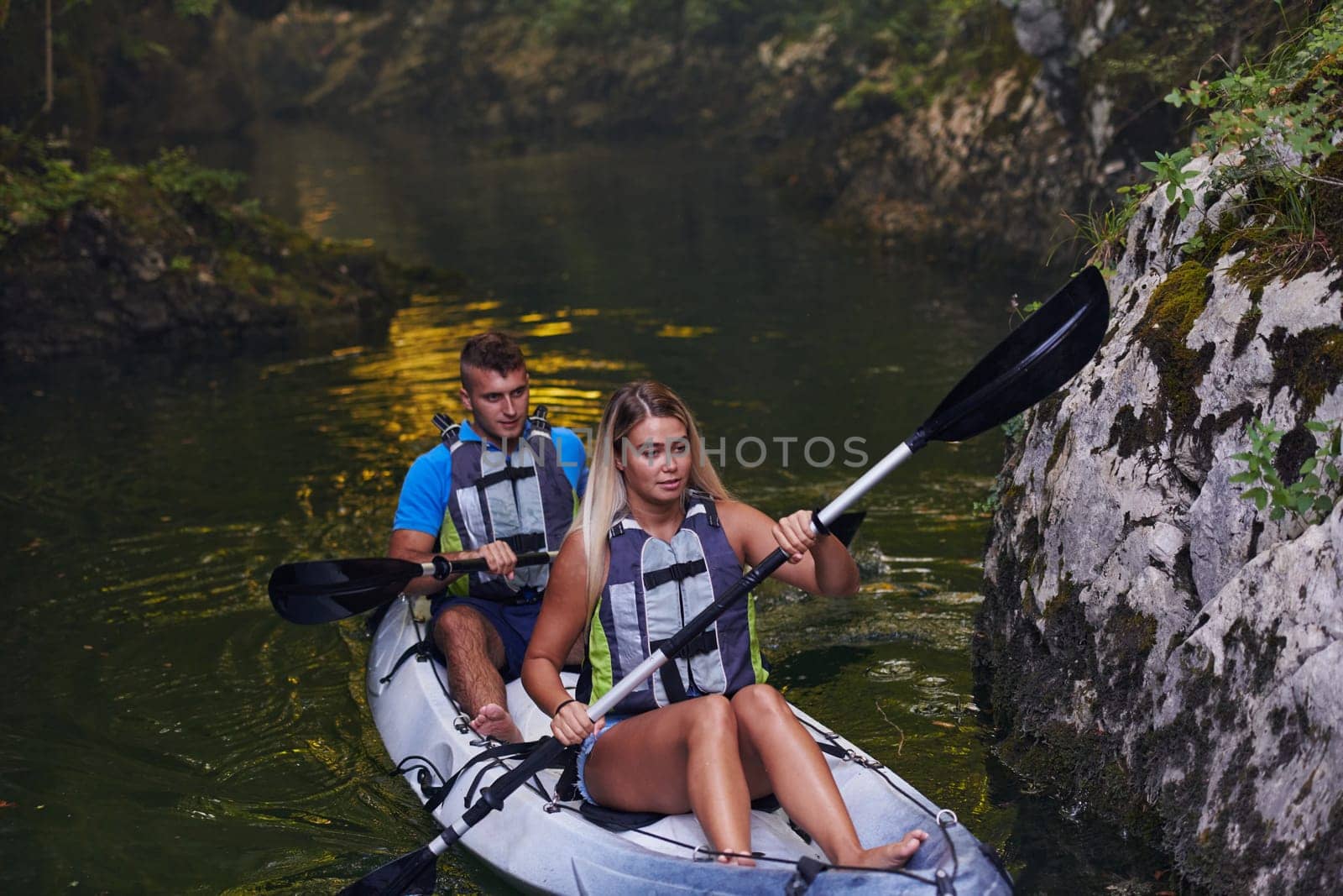 A young couple enjoying an idyllic kayak ride in the middle of a beautiful river surrounded by forest greenery.