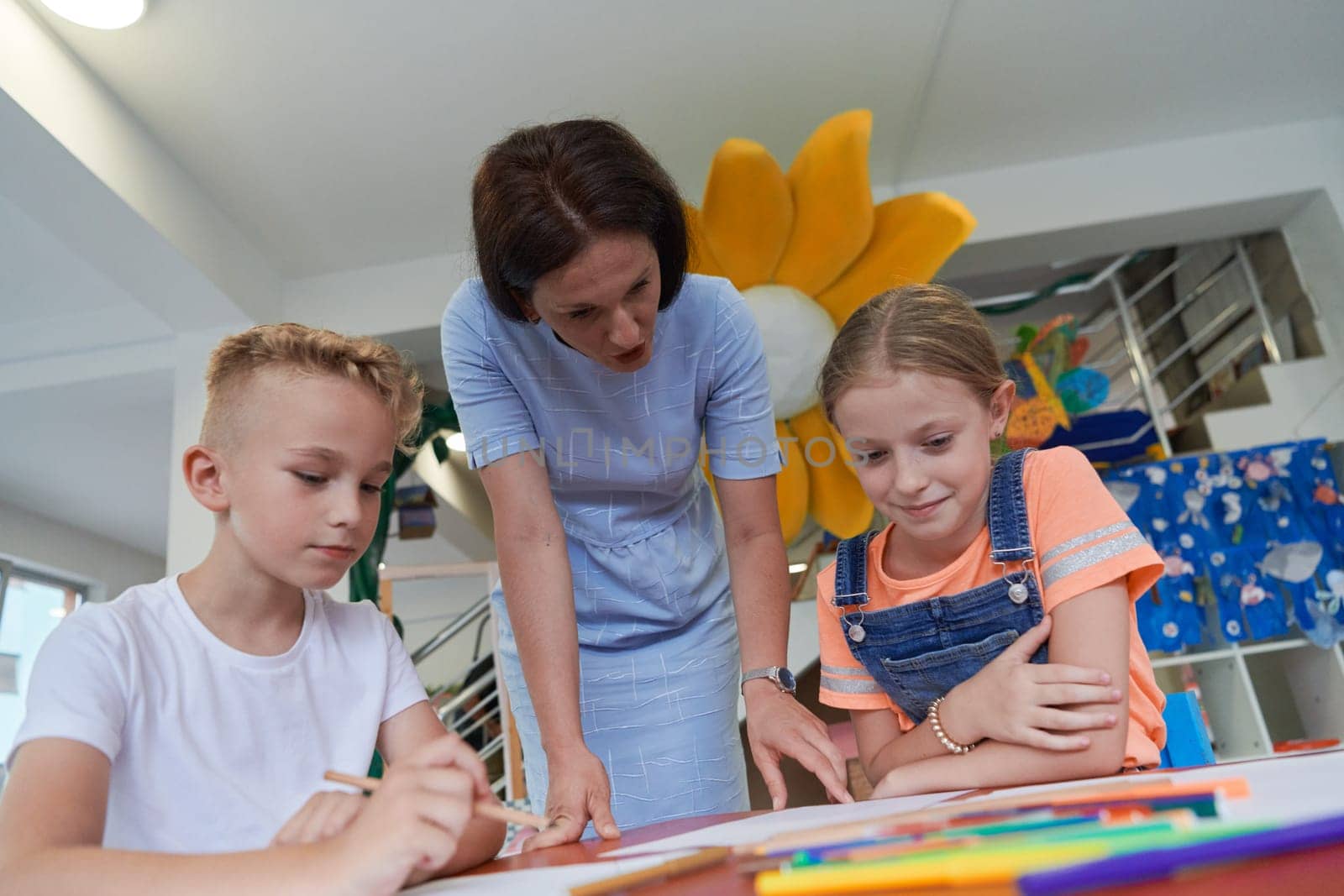 Creative kids during an art class in a daycare center or elementary school classroom drawing with female teacher