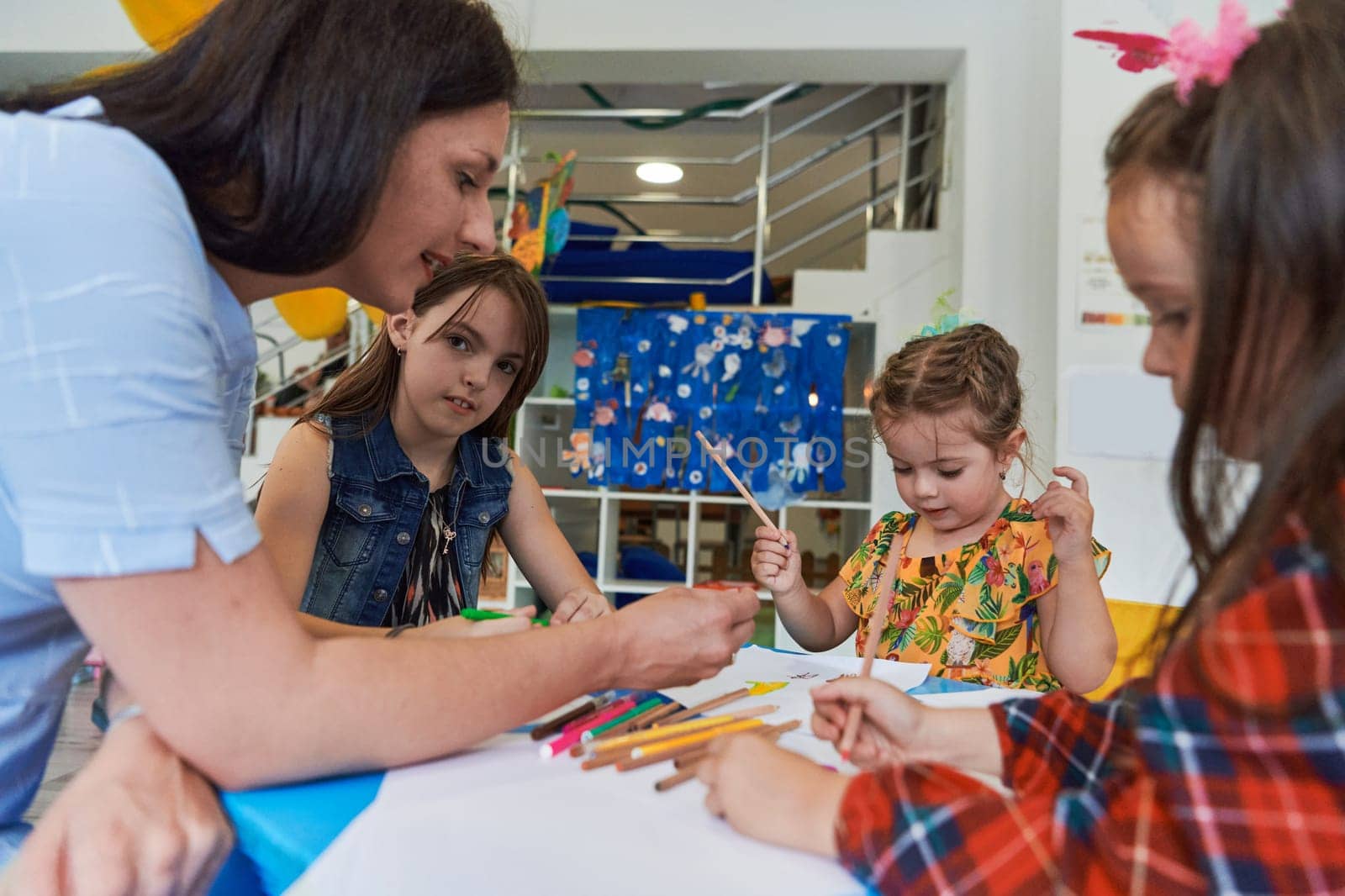 Creative kids during an art class in a daycare center or elementary school classroom drawing with female teacher