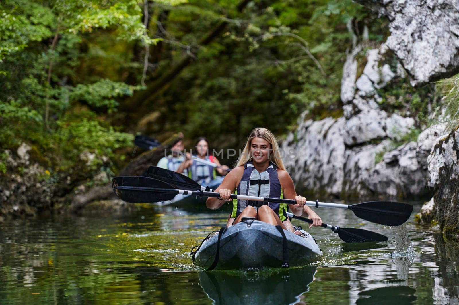 A group of friends enjoying having fun and kayaking while exploring the calm river, surrounding forest and large natural river canyons by dotshock