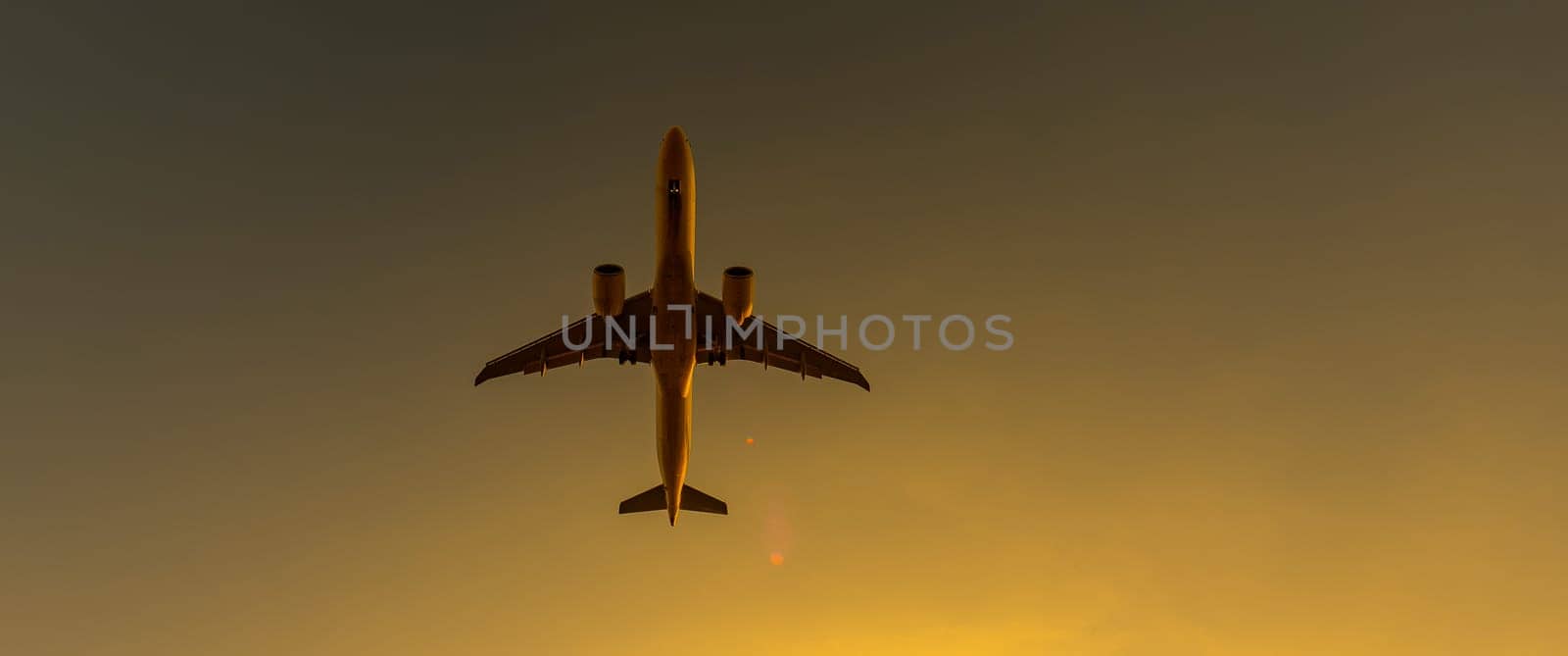 Bottom view of a flying plane at sunset. Widescreen