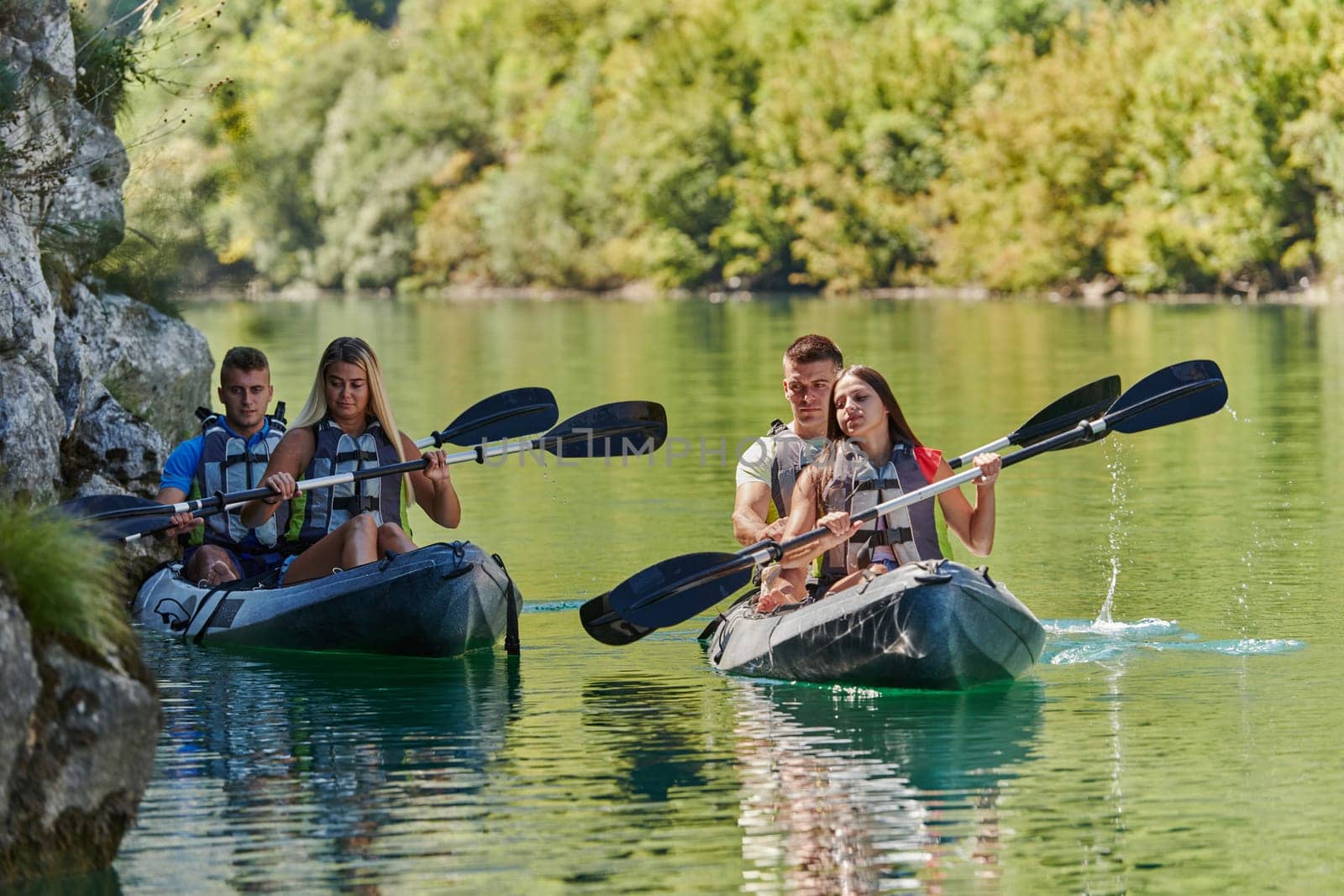 A group of friends enjoying having fun and kayaking while exploring the calm river, surrounding forest and large natural river canyons.