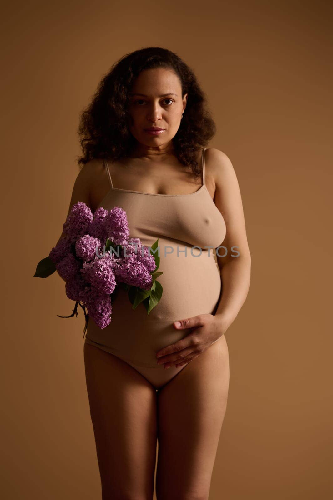 Beautiful pregnant woman holding bunch of purple lilacs, touching her big belly. Femininity. Pregnancy. Body positivity by artgf