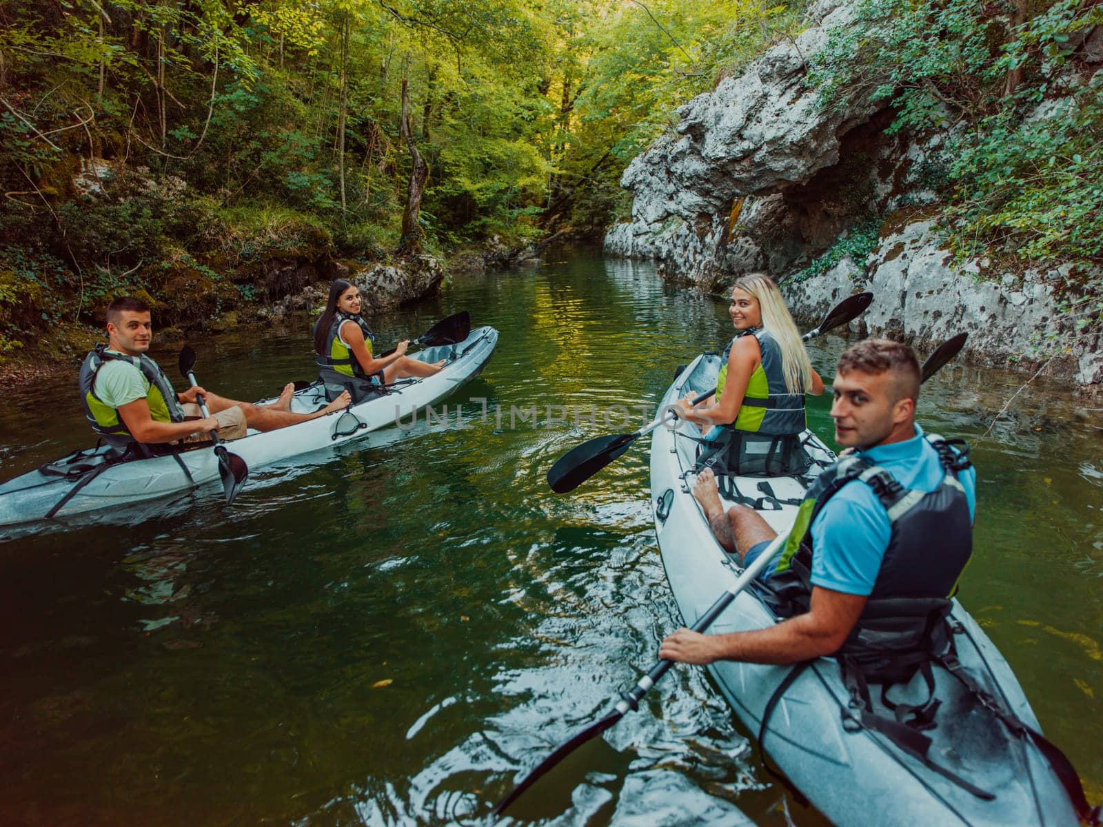 A group of friends enjoying having fun and kayaking while exploring the calm river, surrounding forest and large natural river canyons.