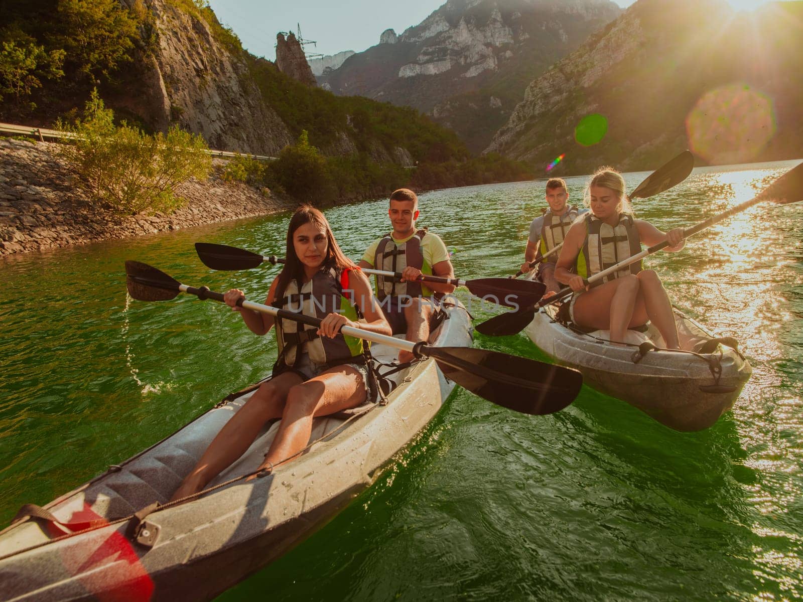 A group of friends enjoying fun and kayaking exploring the calm river, surrounding forest and large natural river canyons during an idyllic sunset. by dotshock