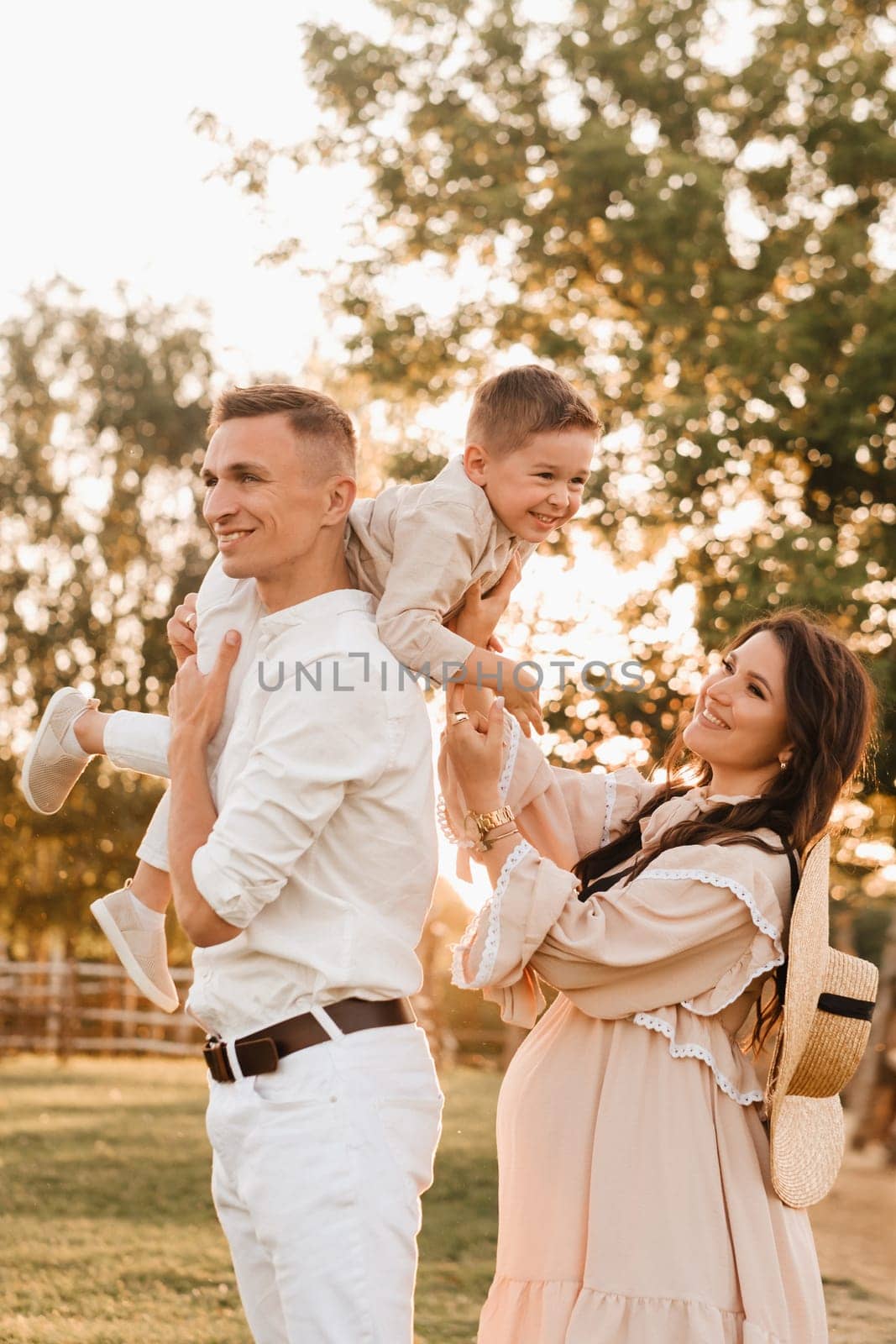 A stylish family in the countryside at sunset. A pregnant woman with her husband and son in nature.