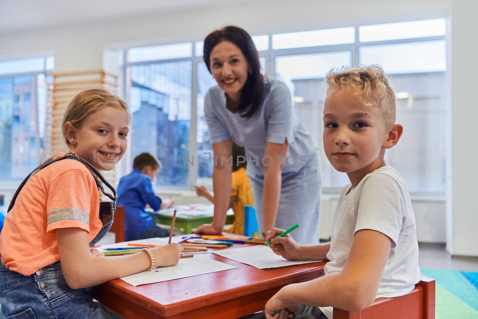 Creative kids during an art class in a daycare center or elementary school classroom drawing with female teacher