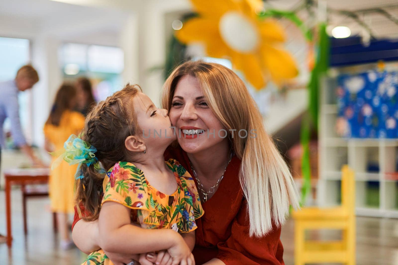 A cute little girl kissing and hugs her mother in preschool by dotshock