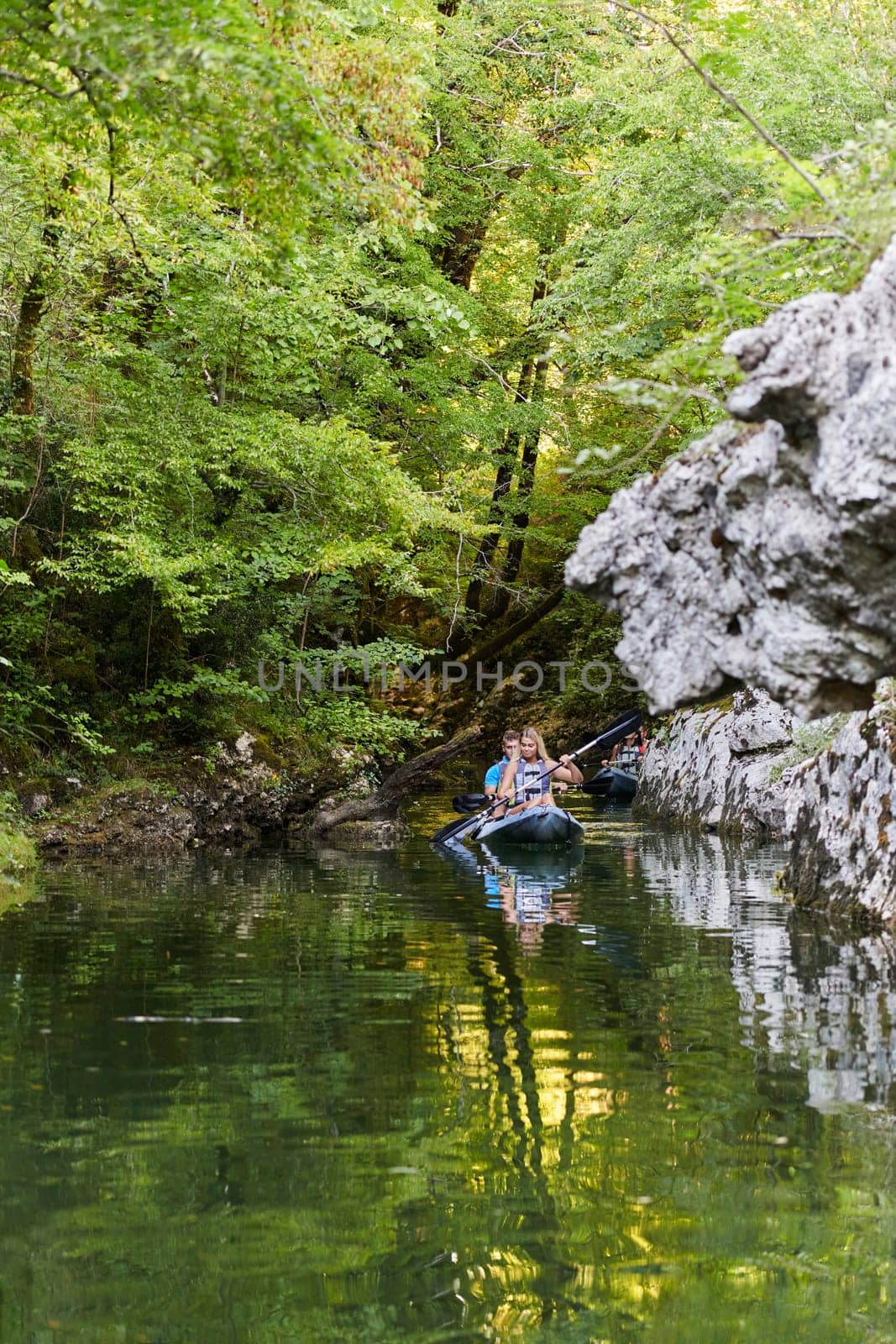 A group of friends enjoying having fun and kayaking while exploring the calm river, surrounding forest and large natural river canyons.