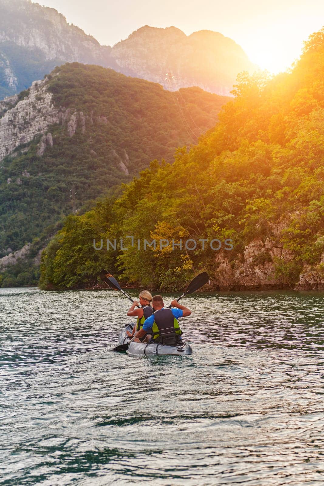 A young couple enjoying an idyllic kayak ride in the middle of a beautiful river surrounded by forest greenery in sunset time by dotshock